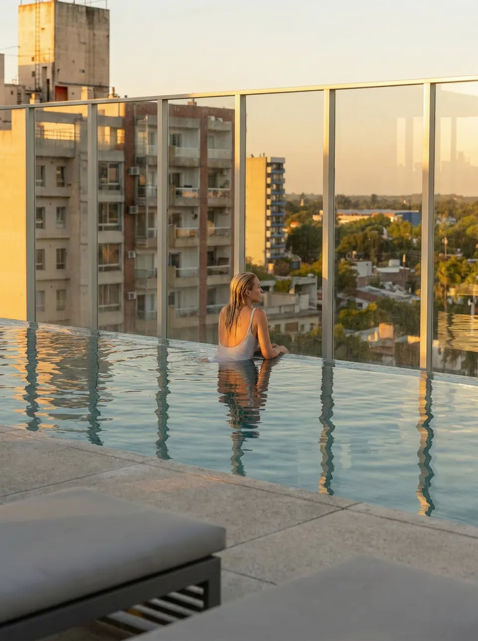 Una mujer en el borde de la piscina infinita, mirando la ciudad al atardecer